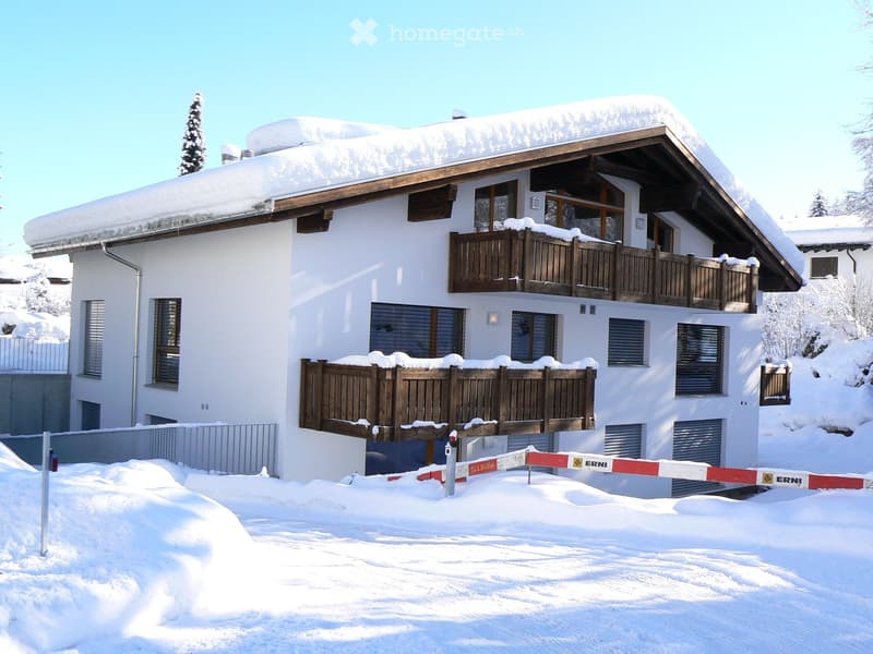 A modern white apartment with snow covered rooftop, balcony, chimney, ground level entrance