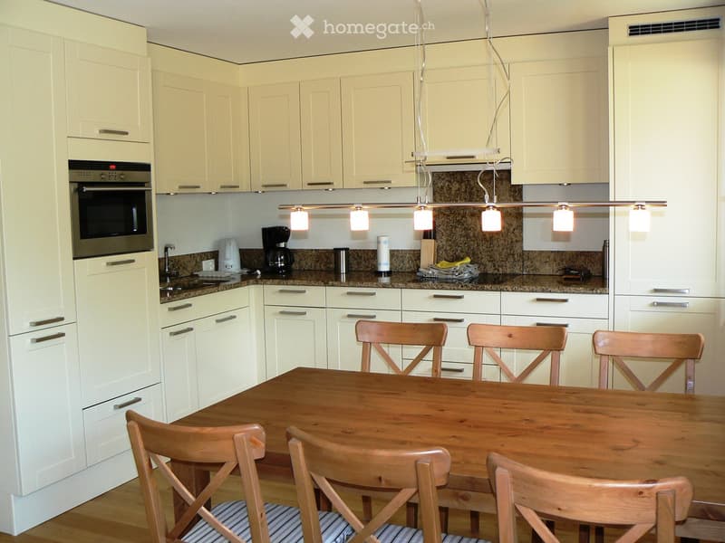 Modern kitchen with wooden table and chairs, cream-colored cabinets, granite countertops, pendant lighting, appliances, faucet, and a large oven.