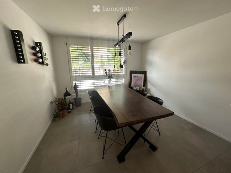 Modern dining area with a large wooden dining table, black chairs, wine rack, and decorative items.