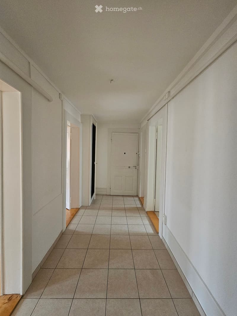 Empty hallway with tiled floor, white walls, and several doors leading to other rooms.