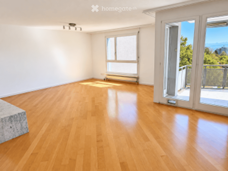 Empty room with light wooden flooring, white walls, large windows, and a sliding glass door leading to a balcony.