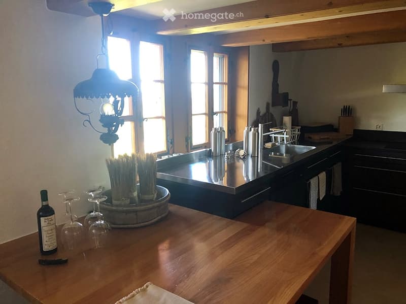 Bright kitchen with wooden table, wine bottle, wine glasses, stainless steel sink, and dark cabinets.