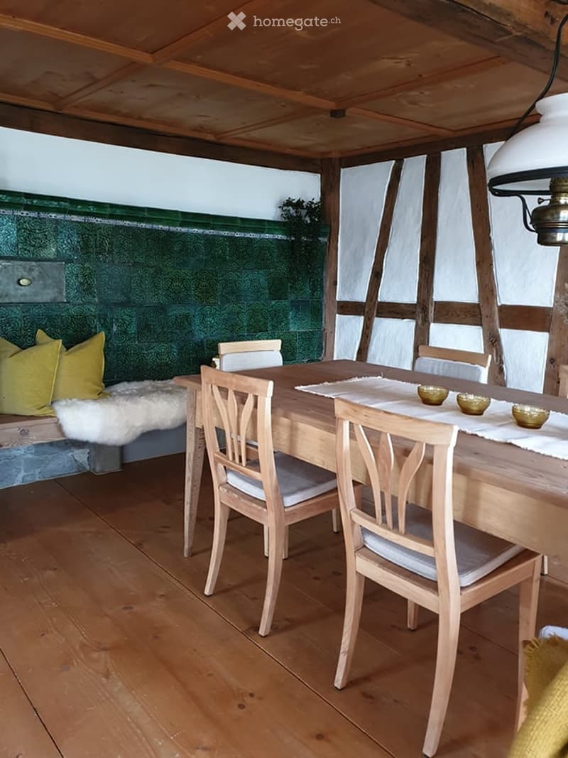 A cozy, wooden-floored dining area with a dining table, chairs, a sofa with pillows, and decorative bowls on the table.