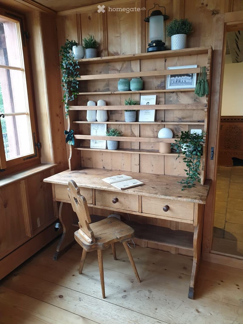 A wooden desk with a chair, shelves filled with books, vases, and plants, and a lantern on top.