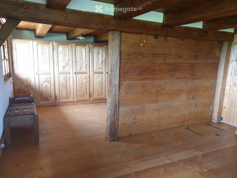 Wooden floor, exposed wooden beams, large wooden wardrobe, small bench with patterned cushion.