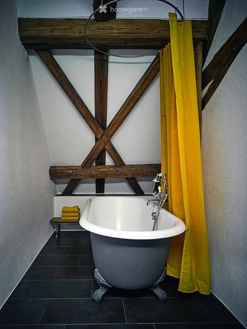 Bathroom with a freestanding clawfoot bathtub, exposed wooden beams, dark tiled floor, and a yellow shower curtain.