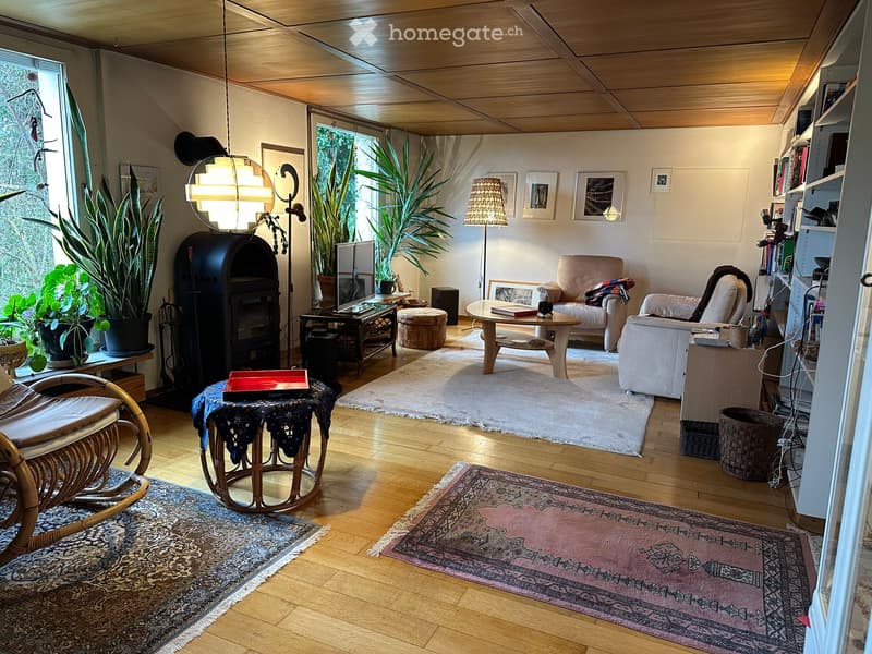 Living room with wooden floor, white walls, large windows, various furniture, plants, and decorative items.