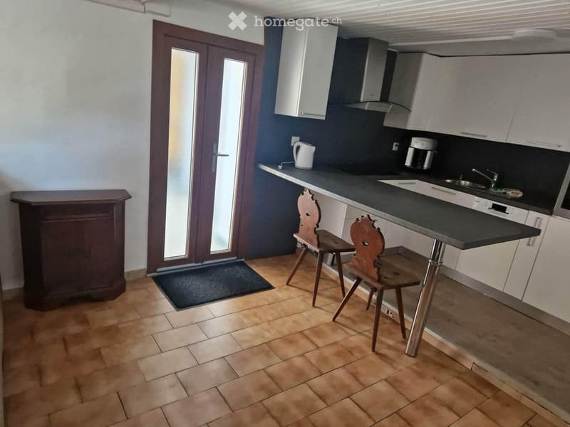 Modern kitchen with wooden tiled floor, white cabinets, black countertop, sink, and two wooden chairs at a small table.