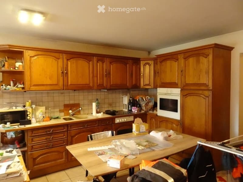 A kitchen with wooden cabinets, a sink, microwave, oven, and a table with chairs.