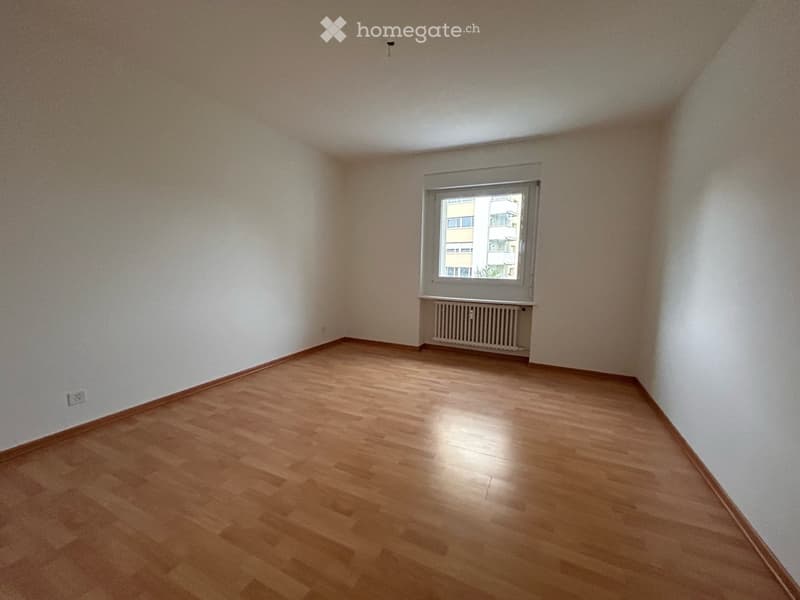 Empty room with wooden flooring, white walls, and a single window with a radiator below it.