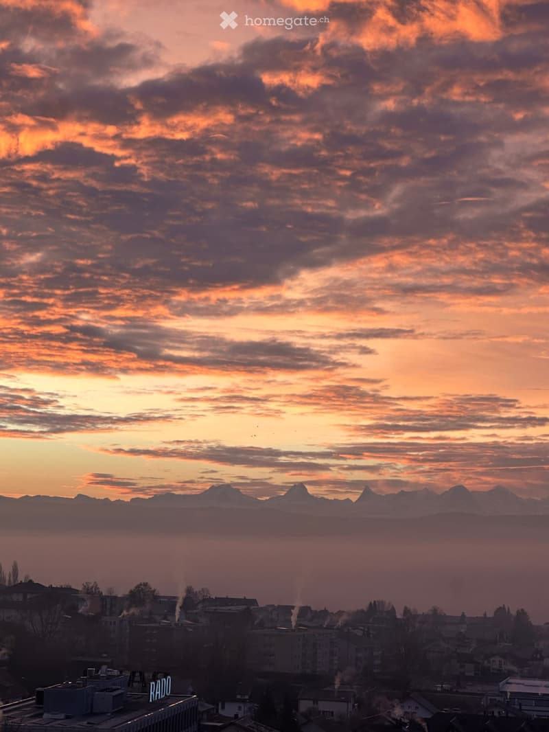 Panoramic view of a cityscape at sunset with mountains in the background and scattered buildings below.