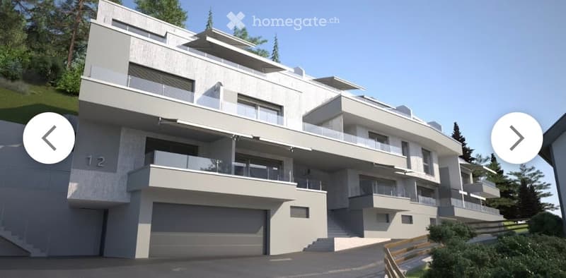 Modern, multi-story residential building with clean lines, large windows, and balconies. Features a prominent garage entrance and is surrounded by greenery.