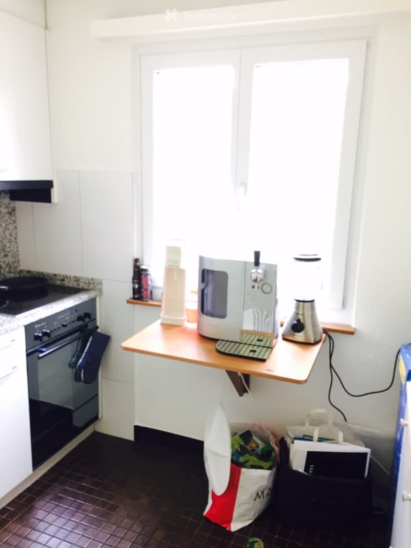 Modern kitchen with white cabinets, a wooden countertop, and various appliances including a microwave, blender, and oven. There are also some bags and items on the floor.