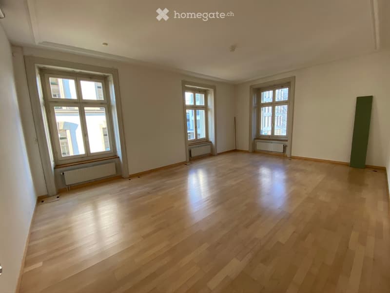 Empty room with wooden flooring, large windows, and radiators under the windows.
