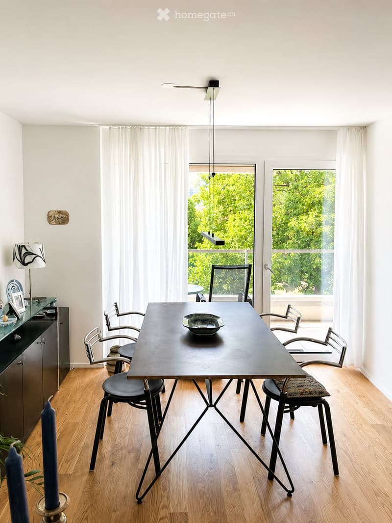 Modern dining room with a dark wooden table, six chairs, a pendant light, and a view of greenery through large windows.