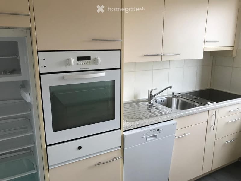 Modern kitchen with light-colored cabinets, stainless steel sink, and white appliances including an oven and dishwasher.
