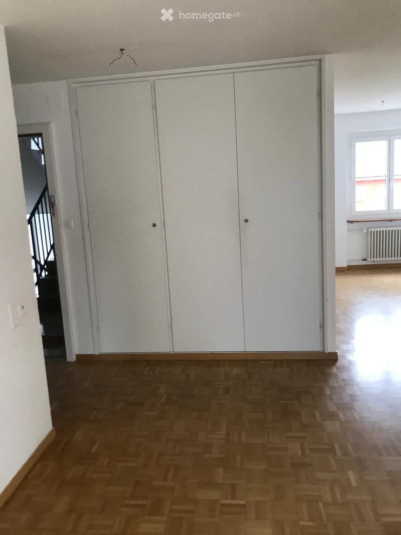 Empty room with wooden flooring, white walls, large built-in closet, and a visible doorway leading to another area.