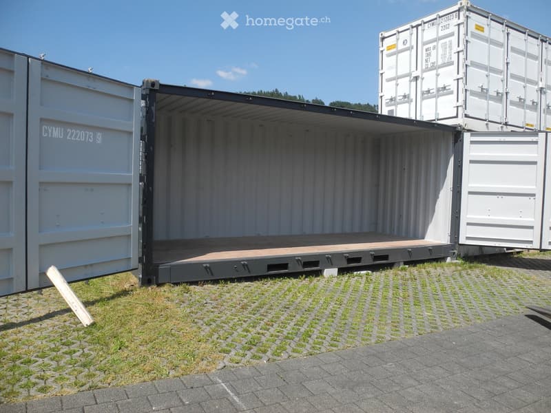 Two large shipping containers with open doors, placed on a paved surface with grass nearby.