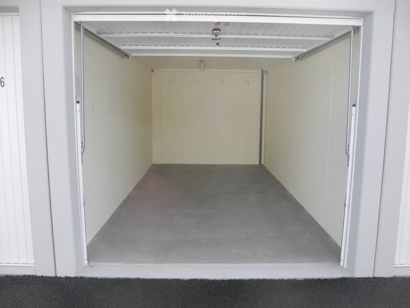 Empty garage with concrete floor, white walls, and overhead storage racks.