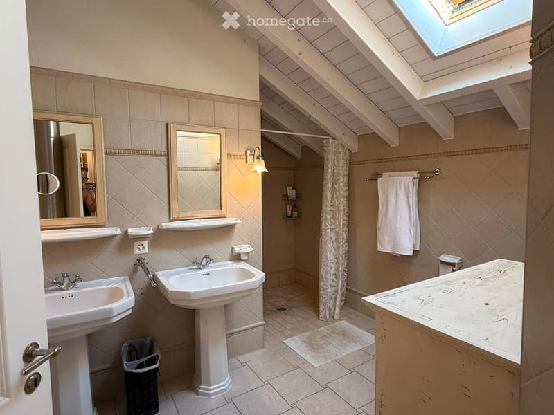 Bathroom with two sinks, mirrors, a toilet, a towel, a shower curtain, and a skylight window.