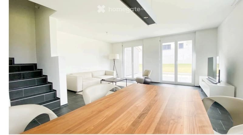 Bright living room with white walls, large sliding glass doors, a white sofa, coffee table, dining table with chairs, and a TV stand.