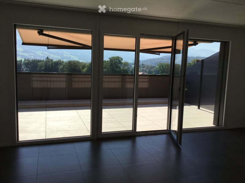 Empty room with large sliding glass doors leading to a balcony or terrace, tiled floor, and a view of greenery and mountains.