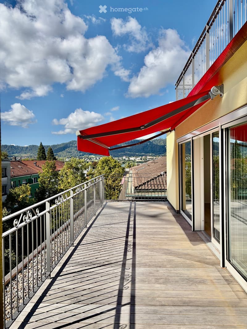 Balcony with wooden decking, metal railing, red awning, scenic mountain view.