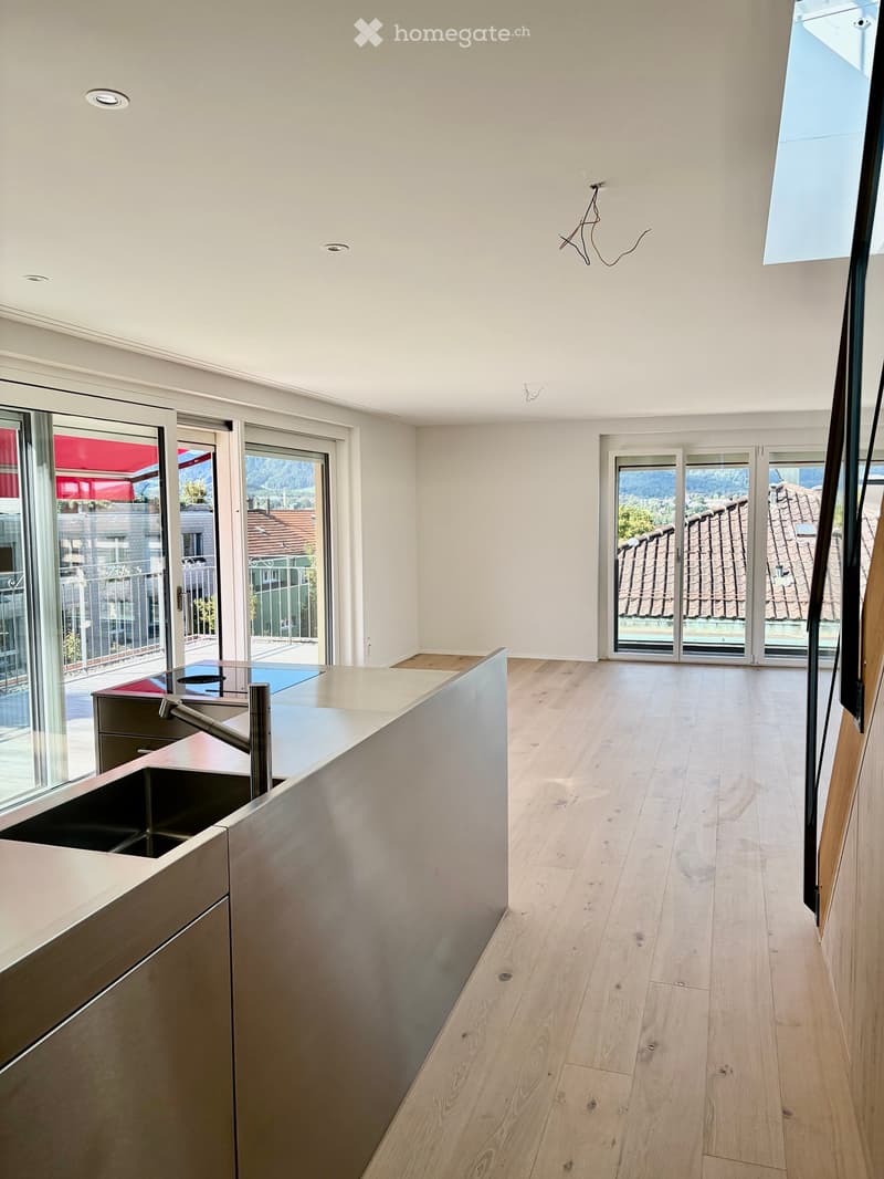 Modern kitchen with light wooden flooring, white walls, and large windows offering a scenic view. Features a sleek, stainless steel sink and faucet.