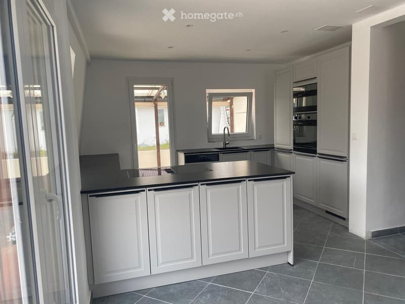 Modern kitchen with white cabinets, black countertop, stainless steel appliances, and large windows offering a view of the outdoor area.