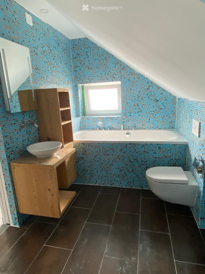 Bathroom with blue mosaic tiles, dark tiled floor, bathtub, toilet, sink, and wooden cabinet.