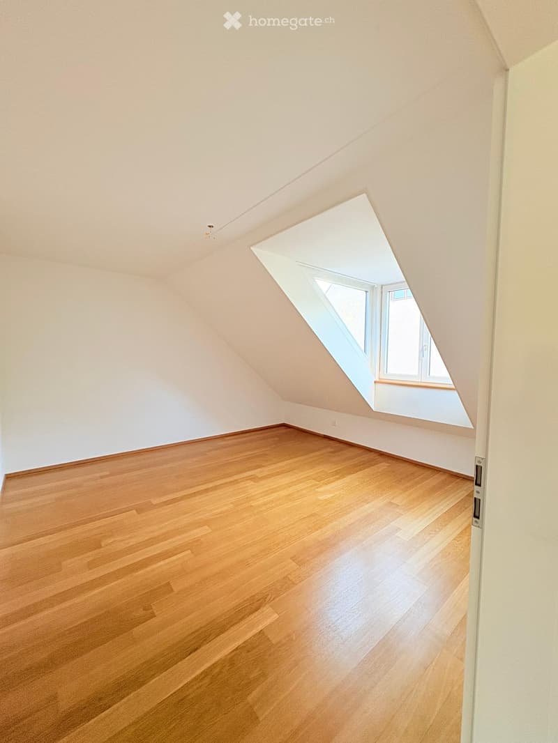 Empty attic room with wooden flooring and a skylight window, featuring white walls and a sloped ceiling.