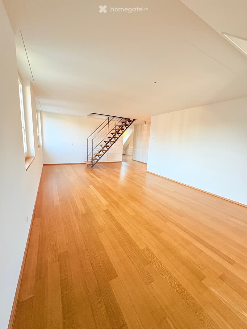 Empty hallway with light wooden flooring, white walls, and a staircase leading upwards.