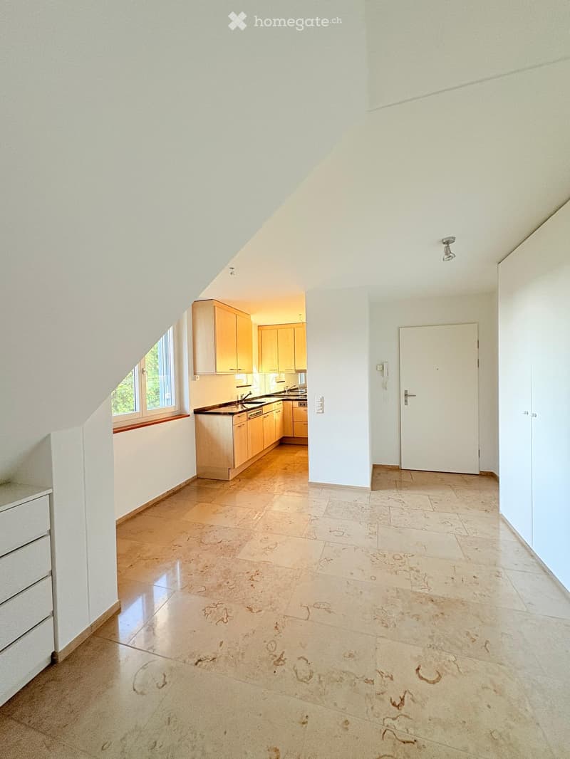 Bright, open room with a kitchen area featuring light wooden cabinets, a sink, and a dishwasher. The floor is tiled with a decorative pattern, and there is a window with a wooden sill on the left side.