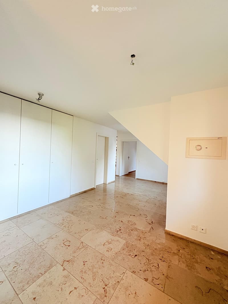 Empty hallway with light-colored tiled flooring, white walls, and two doors leading to other rooms. The hallway features a large mirrored closet on one side and a staircase leading upwards.