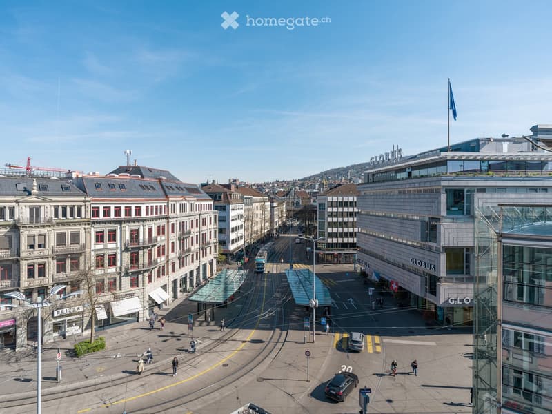 Aerial view of a city with multiple buildings, tram tracks, and people walking on the street.