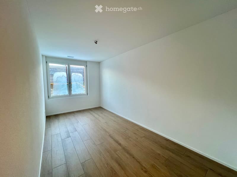 Empty room with light-colored walls and wooden flooring, featuring a single window with frosted glass panels.
