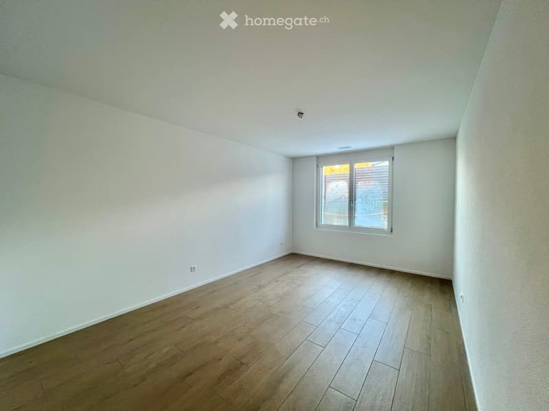 Empty room with light-colored walls and wooden flooring, featuring a single window with blinds.