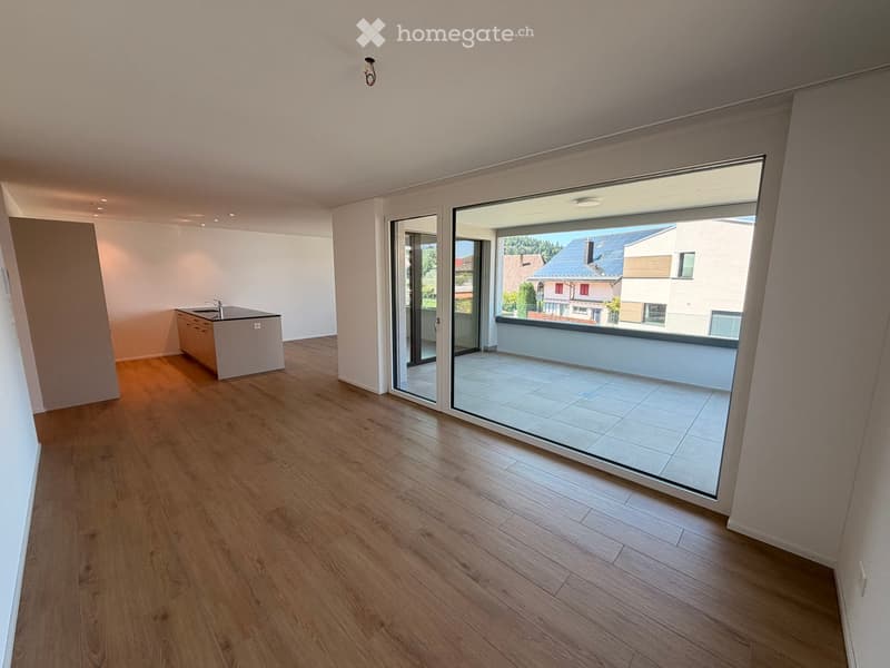 Bright, unfurnished room with wooden flooring, a small kitchen area with a sink and cabinet, and large glass doors leading to a balcony.