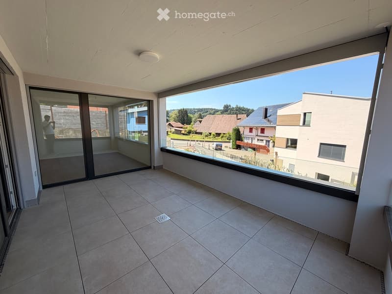 Balcony with tiled floor, large glass sliding doors, and a view of a residential area with houses and greenery.
