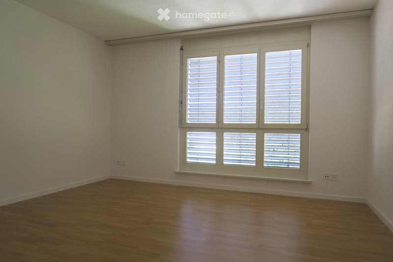 Empty room with wooden flooring, white walls, and large windows with shutters.