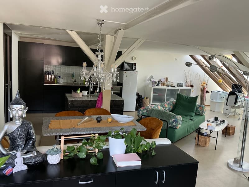 Open-plan living and dining area with a modern sofa, dining table, kitchen area, and decorative items including a Buddha statue and plants.