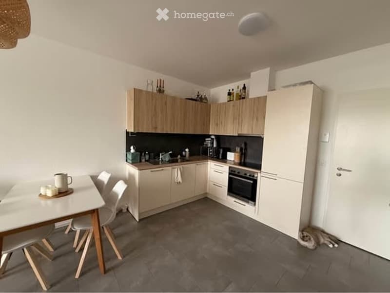 Modern kitchen with light wood cabinets, stainless steel appliances, and a small dining area with a table and chairs.