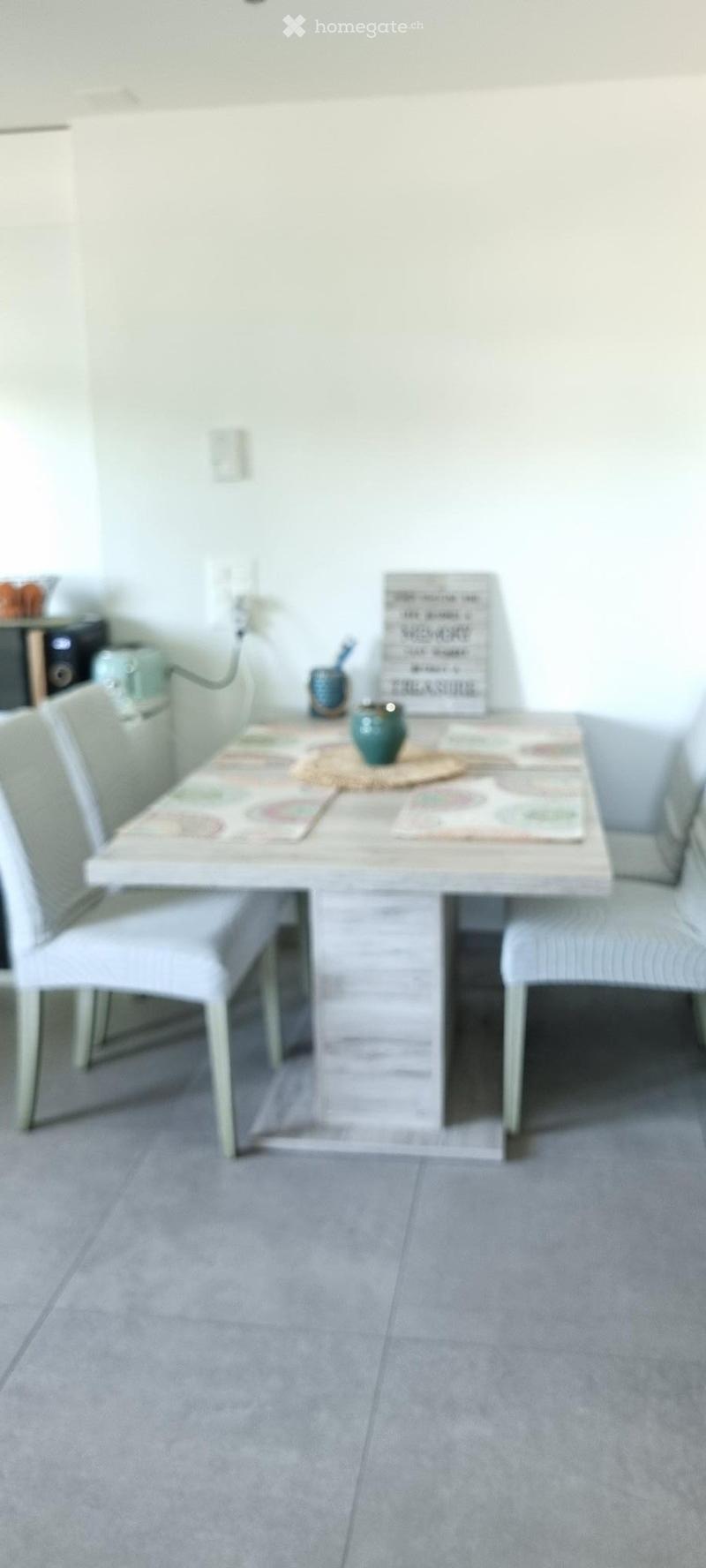 Dining area with a white table, four chairs, a decorative sign, and a small bowl on the table.