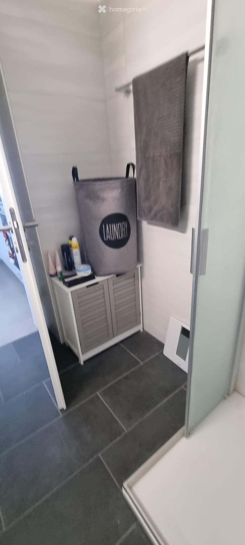 Bathroom with dark tiled floor, white cabinet, laundry basket, and towel hanging on the wall.