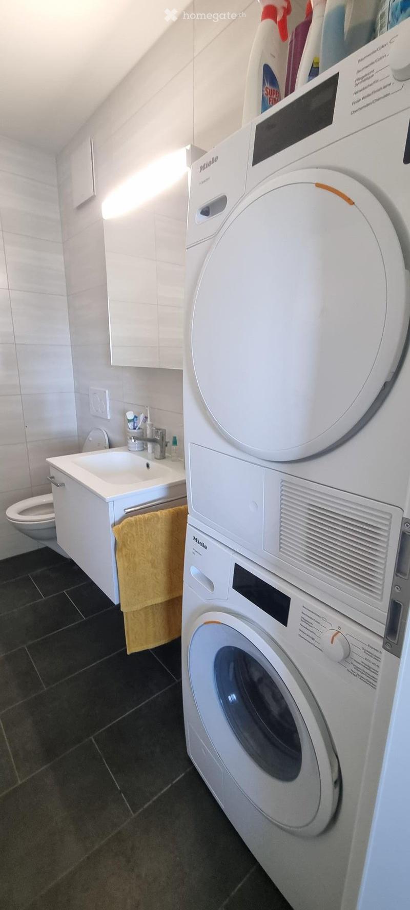 Bathroom with a white sink, toilet, and a stacked washing machine and dryer unit. A yellow towel hangs on the cabinet.