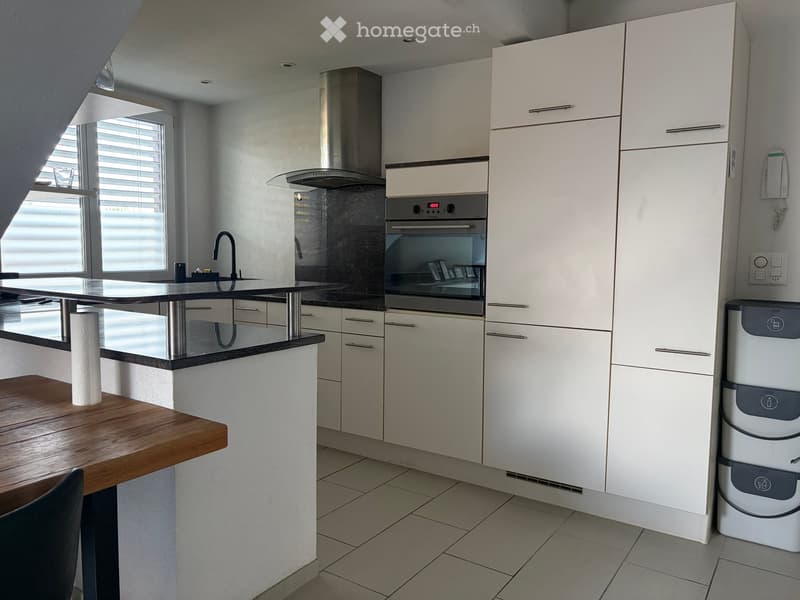 Modern kitchen with white cabinets, stainless steel appliances, a central island with a black countertop, and a wooden dining table with a chair.