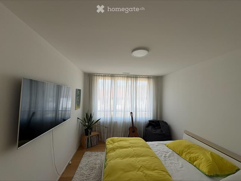 A modern bedroom with a bed, yellow bedding, a guitar, a plant, a small table with a plant, a mirror, and a picture frame on the wall.