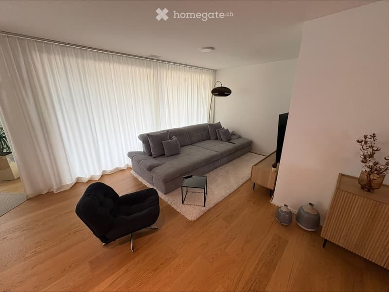 Modern living room with a grey sectional sofa, black armchair, small coffee table, floor lamp, and decorative vases on a side table.