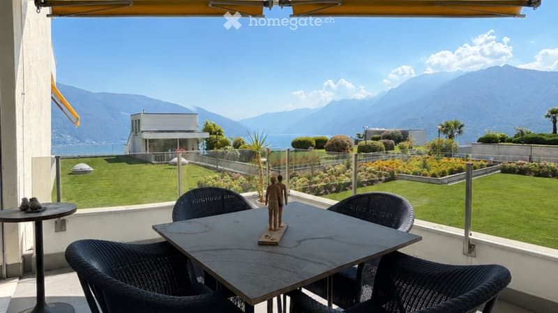 Balcony with a table and chairs, overlooking a well-maintained garden and scenic mountain view.