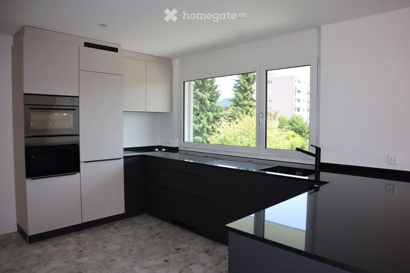 Modern kitchen with white and black cabinets, a stainless steel sink, and an oven. Large windows provide natural light and a view of greenery.